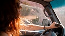 Eine Frau sitzt bei Sonnenschein im Auto. | Bild: mauritius-images