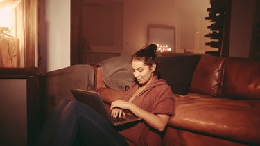 Frau relaxt mit ihrem Laptop im Wohnzimmer | Bild: mauritius-images