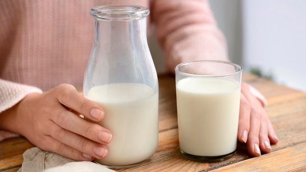 Frau hält eine Flasche Milch und ein Glas in der Hand auf einem Tisch | Bild: mauritius images