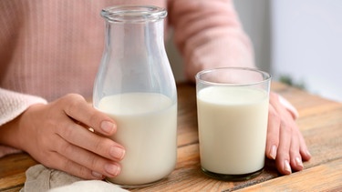 Frau hält eine Flasche Milch und ein Glas in der Hand auf einem Tisch | Bild: mauritius images / Pixel-shot / Alamy / Alamy Stock Photos
