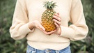 Eine Frau hält eine Ananas in beiden Händen | Bild: mauritius images / Westend61 / Pau Cardellach Lliso