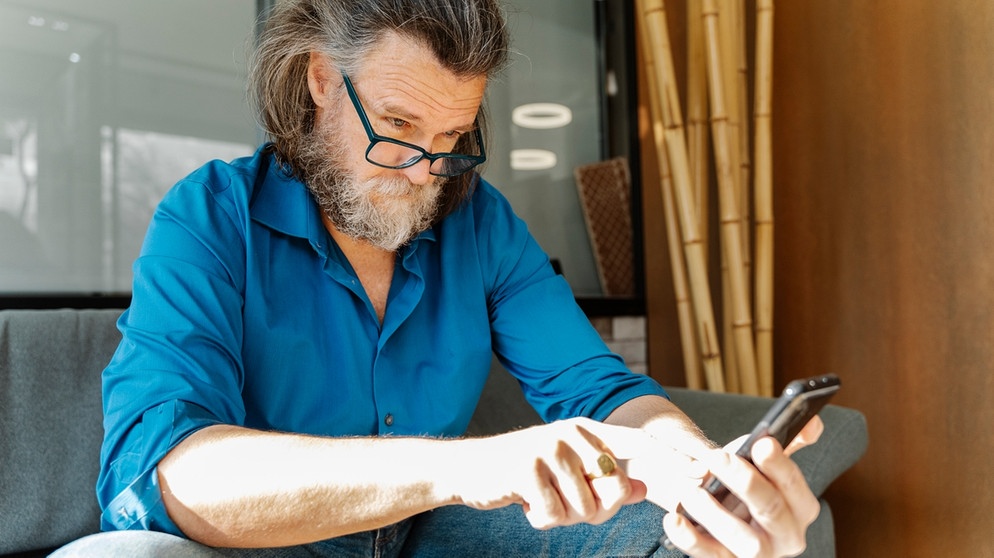 Ein Mann blickt skeptisch auf sein Handy | Bild: mauritius-images