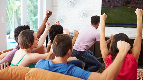 Freunde sitzen vor einem Fernseher und sehen sich ein Fussballspiel an. | Bild: mauritius images