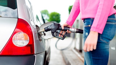 Frau füllt an einer Tankstelle Kraftstoff in ihr Auto. | Bild: mauritius images