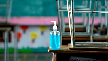 In einem leeren Klassenzimmer steht einsam eine Flasche Desinfektionsmittel | Bild: mauritius-images