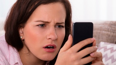 Frau schaut erschreckt auf ihr Handy | Bild: mauritius-images
