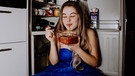 Eine Frau im Ballkleid sitzt vor dem Kühlschrank und isst  | Bild: Picaro Photography