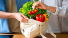 Hand holt aus einer Einkaufstasche mit Gemüse eine Rispe Tomaten heraus | Bild: mauritius images
