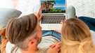 Paar sitzt auf einem Sofa und plant seinen Urlaub | Bild: mauritius images / György Barna / Alamy / Alamy Stock Photos