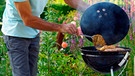 Ein Mann grillt Fleisch im Garten auf einem Kugelgrill | Bild: mauritius images