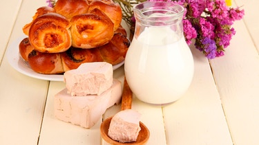 Ein Teller Hefegebäck stehen mit einer Kanne Milch und einem Frischhefewürfel auf einem weißen Holztisch | Bild: mauritius images / Pixel-shot / Alamy / Alamy Stock Photos