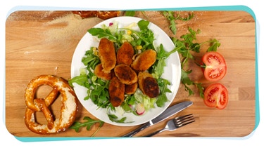 Panierte und gebackene Weißwurst-Radel liegen auf einem Salatbett auf einem Teller. | Bild: BR