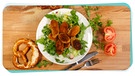Panierte und gebackene Weißwurst-Radel liegen auf einem Salatbett auf einem Teller. | Bild: BR