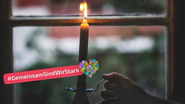 Hand stellt brennende Kerze in einem Kerzenhalter ins Fenster. | Bild: mauritius images