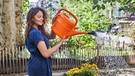 Eine Frau gießt ihren Garten mit einer orangen Gießkanne | Bild: mauritius-images