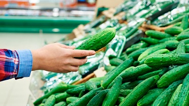 Eine Hand hält eine Salatgurke im Supermarkt | Bild: mauritius-images