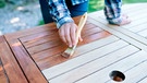 Hand mit einem Pinsel streicht einen Gartentisch | Bild: mauritius images