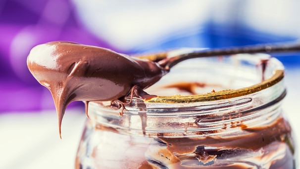Löffel mit Schoko-Nusscreme liegt auf einem geöffneten Glas des Aufstrichs. | Bild: mauritius images