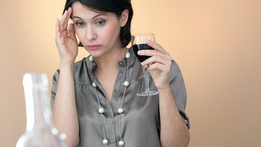 Eine Frau hält ein Glas Rotwein in der Hand und hat Kopfweh | Bild: mauritius images