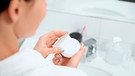 Frau hält im Badezimmer eines Hotels eine Creme-Probe in de Händen | Bild: mauritius images