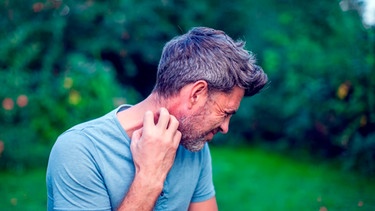 Mann steht in einem Garten und kratzt sich am Hals | Bild: mauritius images