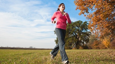 Eine Frau joggt über eine Wiese im Herbst. | Bild: mauritius images
