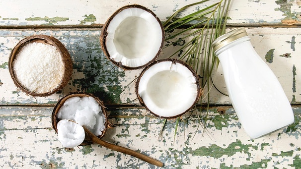 Verschiedene Kokosprodukte wie Kokosflocken, Kokosmilch und Kokosöl in Kokosschalen auf einer Holzunterlage | Bild: mauritius images