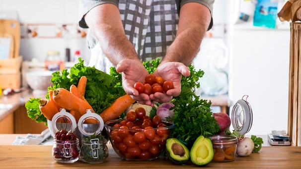 Mann zeigt in einer Küche seine Gemüseeinkäufe | Bild: mauritius images