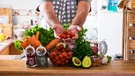Mann zeigt in einer Küche seine Gemüseeinkäufe | Bild: mauritius images