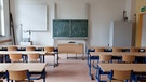 Ein leeres Klassenzimmer mit Blick auf Tafel und Lehrerpult. | Bild: stock.adobe.com/PRCreativeTeam
