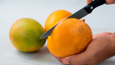 Hand hält Mango und schneidet sie auf | Bild: mauritius images / Julio Rivalta / Alamy / Alamy Stock Photos