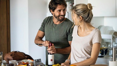 Mann öffnet eine Flasche Rotwein in einer Küche | Bild: mauritius images