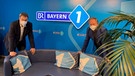 Ministerpräsident Markus Söder und BAYERN 1 Moderator Thorsten Otto stehen an der Blauen Couch im Studio von BAYERN 1 | Bild: BR