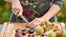 Frau ritzt mit einem Messer eine Esskastanie ein | Bild: mauritius images