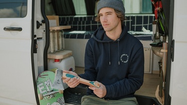 Moritz Bacher sitzt in seinem Bus und hält eine Axt, deren Griff aus alten Skateboards entstand | Bild: Magazin Himmeblau, Andreas Jakob