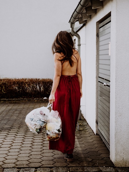 Eine junge Frau bringt im roten Ballkleid den Müll zur Tonne. | Bild: Picaro Photography
