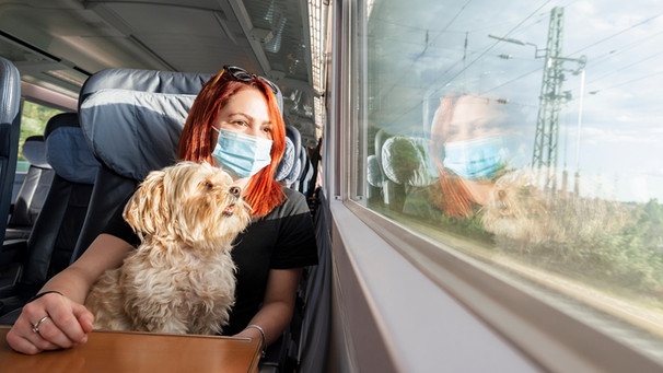 Rothaarige Frau sitzt mit Hund und Maske im Zug | Bild: mauritius-images