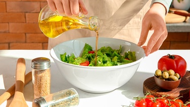 Frau bereitet einen Salat mit Olivenöl zu. | Bild: mauritius images