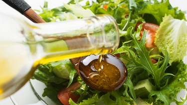 Olivenöl fließt aus einer Flasche über Salat | Bild: mauritius images / foodcollection