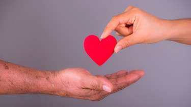 Eine Hand legt ein symbolisches Herz in eine andere Hand. | Bild: mauritius images / PHONGSAKORN PORNSUPARAK / Alamy / Alamy Stock Photos