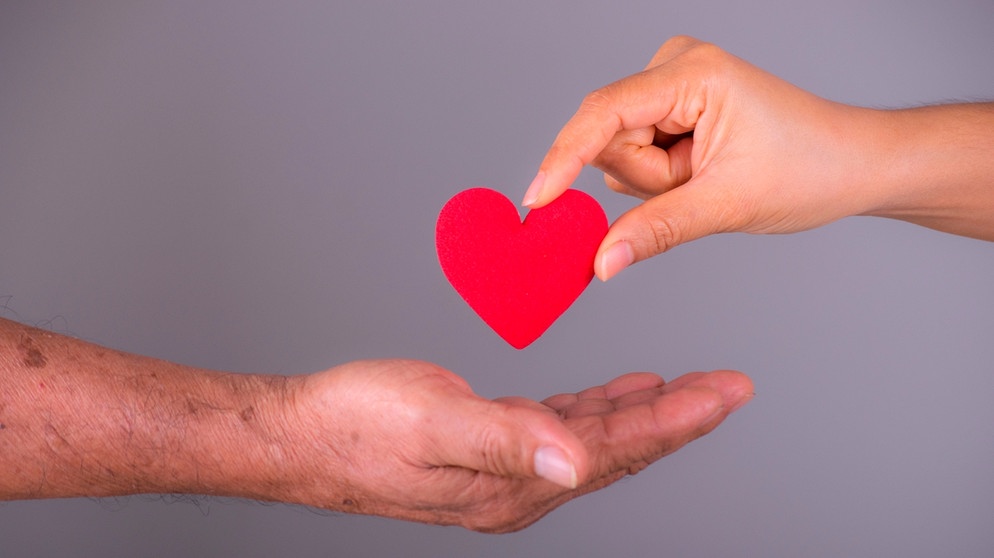 Eine Hand legt ein symbolisches Herz in eine andere Hand. | Bild: mauritius images / PHONGSAKORN PORNSUPARAK / Alamy / Alamy Stock Photos