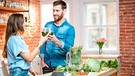 Ein Paar trinkt in der Küche einen grünen Smoothie. | Bild: mauritius images / RossHelen editorial / Alamy / Alamy Stock Photos