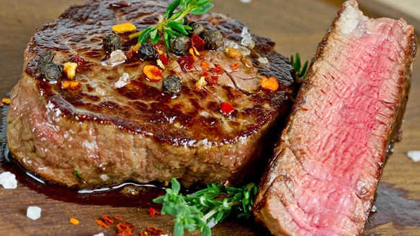 Auf einem Holzbrett liegt ein in Scheiben geschnittenes Steak medium rare . | Bild: mauritius-images