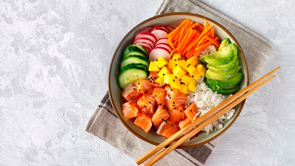 Eine Poké-Bowl mit Radieschen, Karotten, Gurke, Avocado und Lachs-Sashimi auf einem Reisbett. | Bild: mauritius-images
