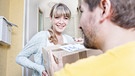 Paketbote übergibt einer Frau ein Paket an der Wohnungstür | Bild: mauritius images