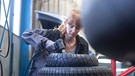 Automechanikerin kontrolliert Reifen in einer Werkstatt | Bild: mauritius images / Westend61 / Sigrid Gombert