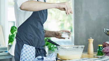 Mann salzt Gericht in einer Küche. | Bild: mauritius images