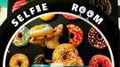 Frau mit Riesen-Donut vor Donut-Wand im SelfieRoom in Mailand | Bild: SelfieRoom, Mailand