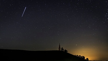 Eine Sternschnuppe fliegt über dem Ridmonument im Allgäu. | Bild: mauritius images / Martin Zurek