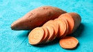 Auf einem hellblauen Untergrund liegen zwei Süßkartoffeln. Eine davon ist zur Hälfte in Scheiben geschnitten. | Bild: mauritius-images